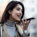 Pretty young woman using voice recognition system on her smartphone while standing in the street.