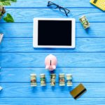Digital tablet with piggy bank and money on blue wooden table