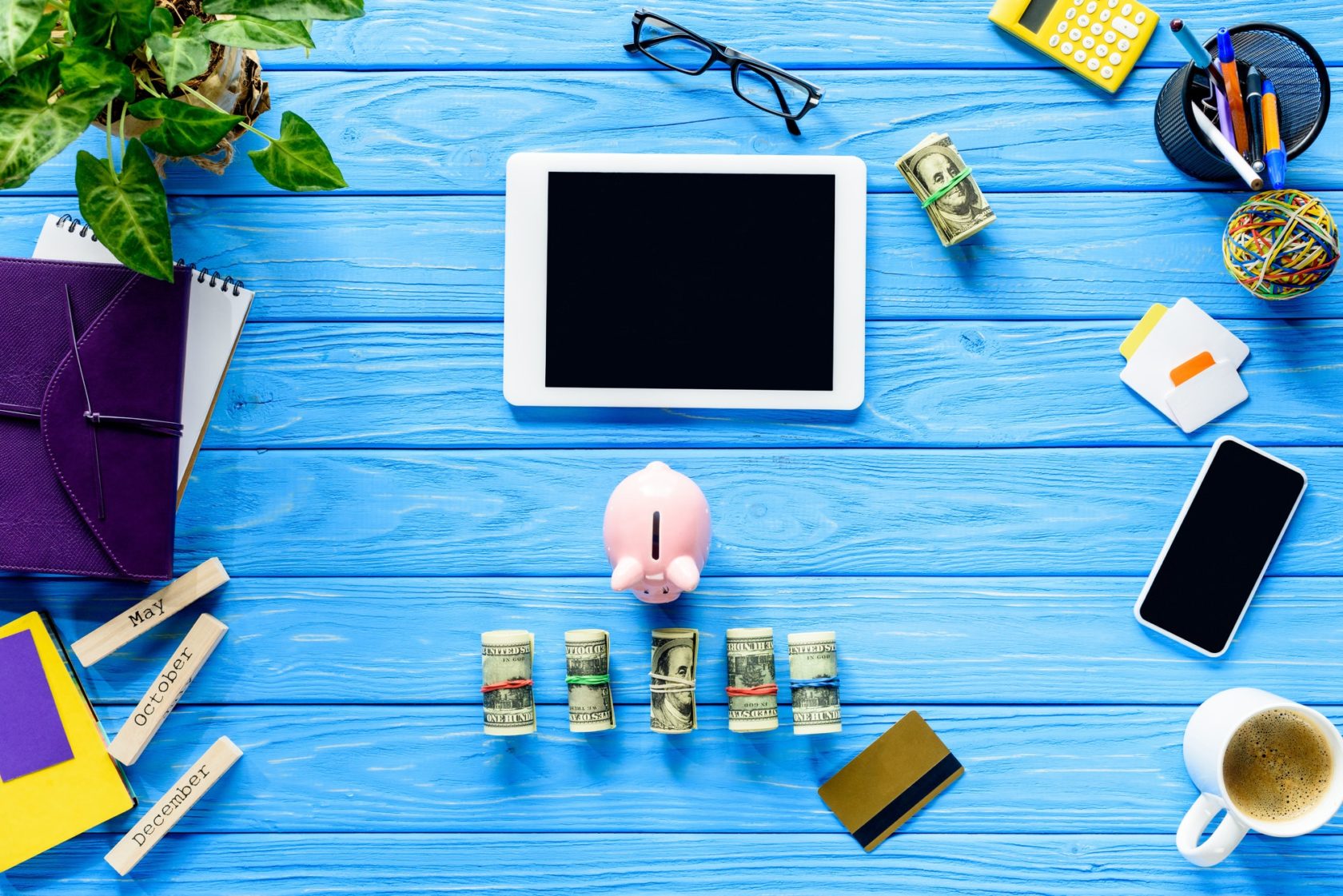 Digital tablet with piggy bank and money on blue wooden table