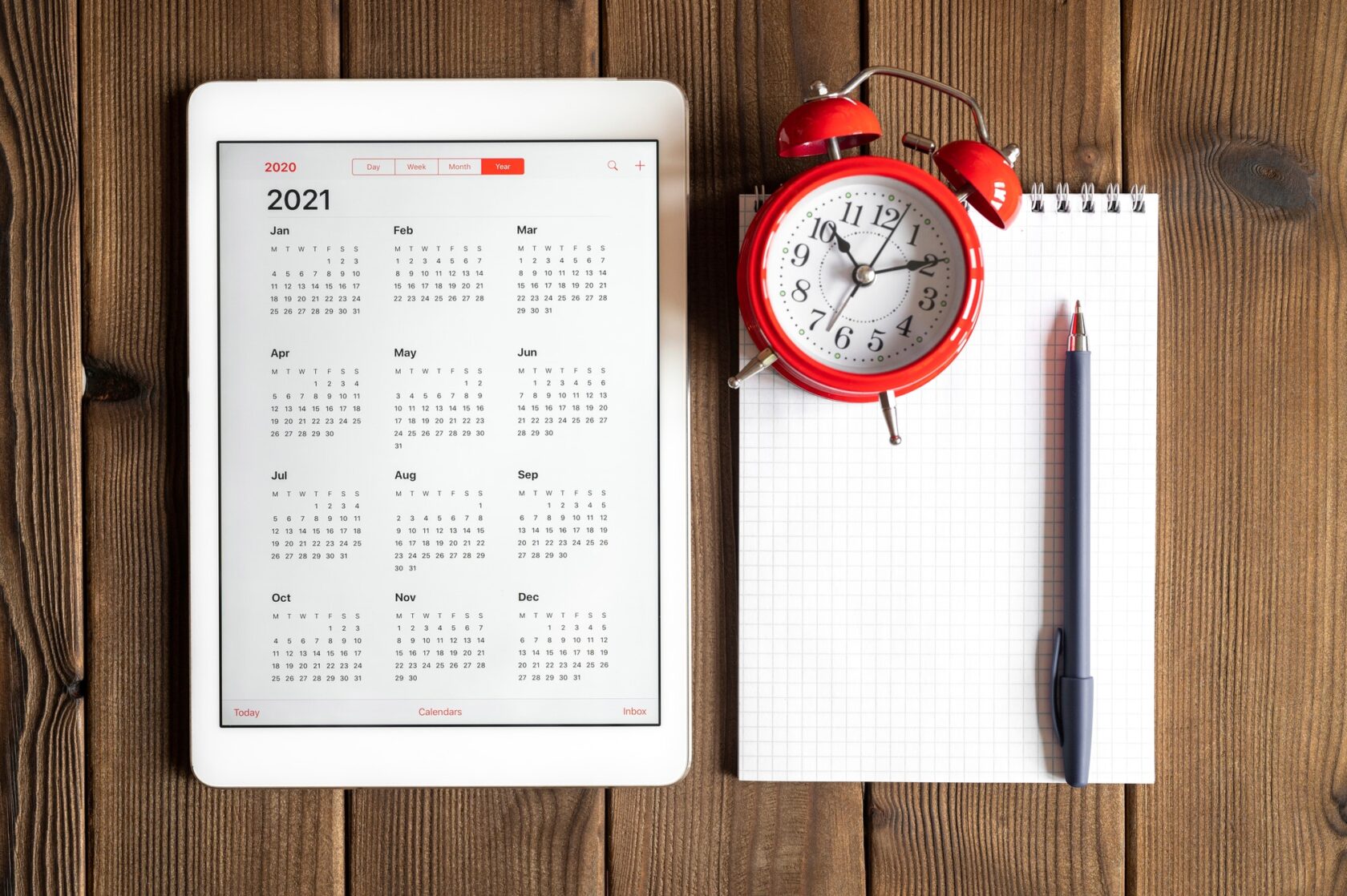 tablet with calendar for 2021, alarm clock and a spring notebook on a wooden background flat lay