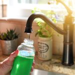 Woman filling reusable eco-friendly glass water bottle in sink, environmentally friendly container