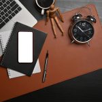 Above view smart phone, laptop, notebook and clock on black table.