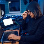Hacker in hood at his workplace, corporate hacking