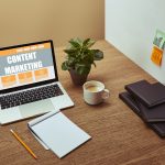 laptop with”content marketing” lettering on screen, notebooks and pencil on wooden tabletop,