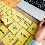 cropped view of woman touching sticky note with seo lettering near laptop on desk