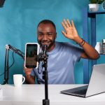 Content creator doing greeting hand gesture in front of live video podcast setup sitting at desk