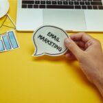 cropped image of man holding speech bubble with”email marketing” lettering near laptop
