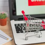 Online shopping concept. Laptop with sale sign on the screen and toy trolley on office desk