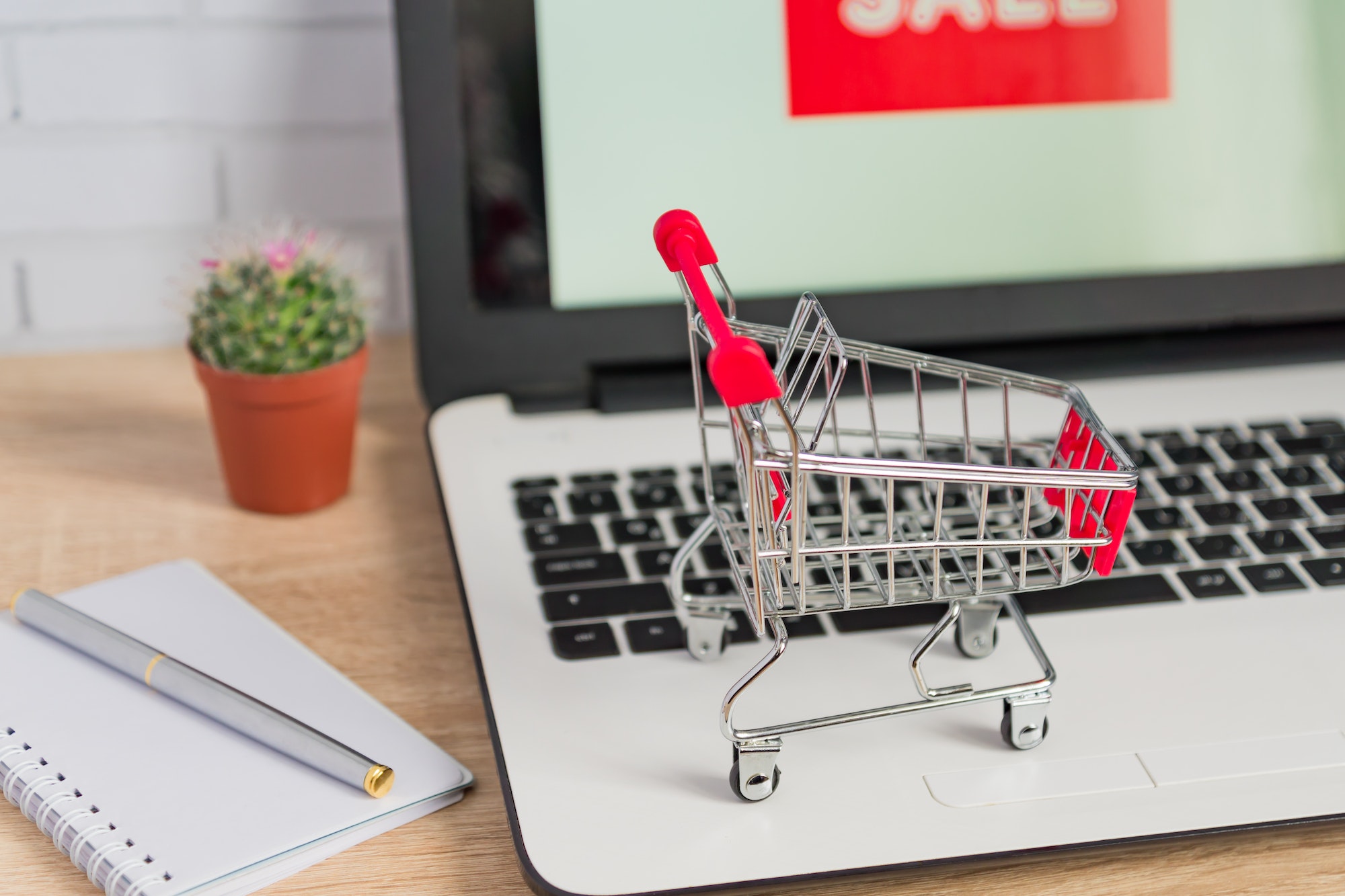 Online shopping concept. Laptop with sale sign on the screen and toy trolley on office desk