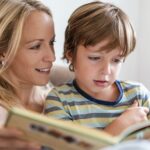 Mother and son reading a book together on couch at home