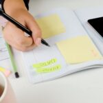 Girl Hands With Mobile Phone With Calendar Writing And List Of Work In Diary On Desk