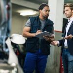 African American car repairman taking notes while talking to a customer at workshop.