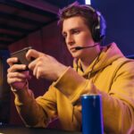 Young pro gamer playing in online mobile video games in neon coloured room