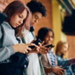Group of teenagers using mobile phones in hallway at high school.