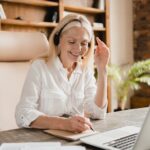 IT support agent, secretary wearing headset taking notes while talking helping clients using laptop