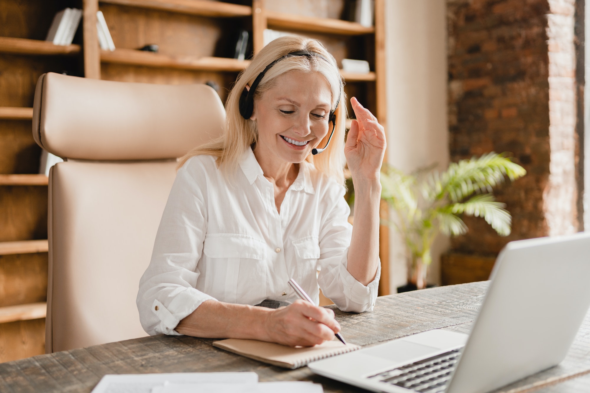 IT support agent, secretary wearing headset taking notes while talking helping clients using laptop