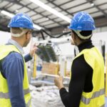 multiracial engineer colleagues checking operation of robotic arm in factory