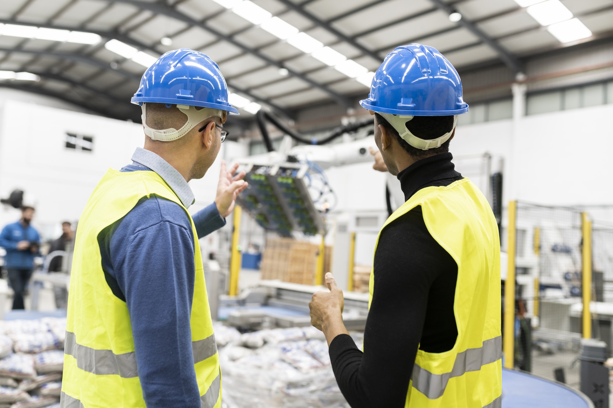 multiracial engineer colleagues checking operation of robotic arm in factory