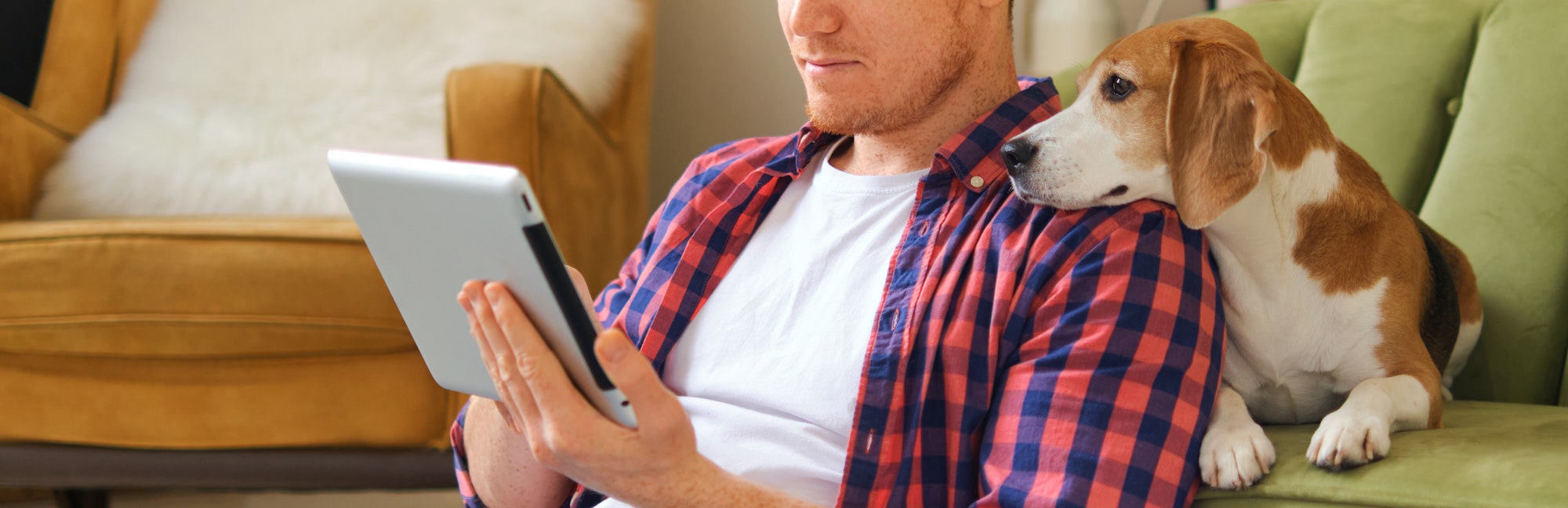 man swipes through a tablet, while his intrigued dog leans in, resting its head on the man's